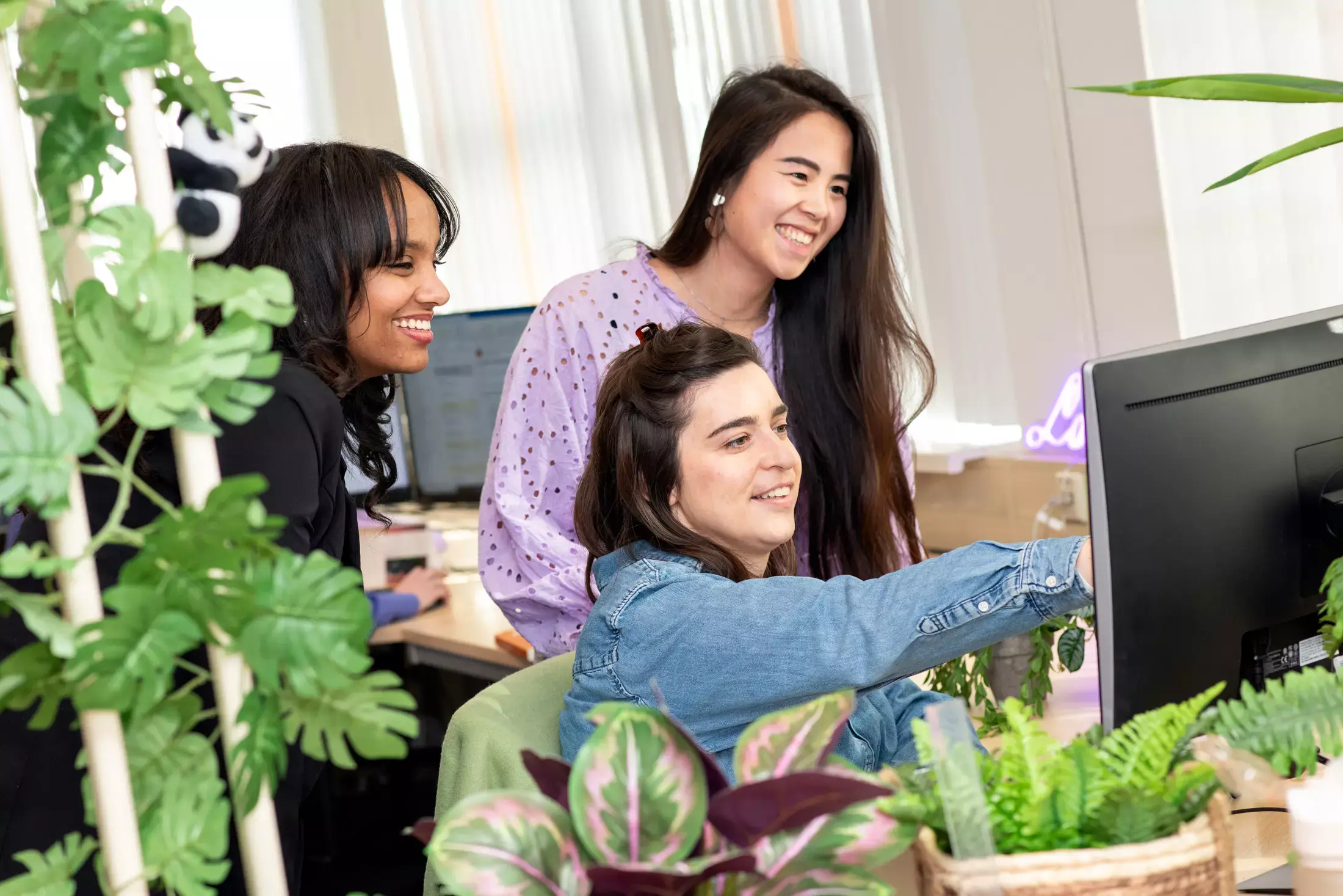 Een jonge medwerker in een winkel staat achter een tafel en vouwt denim broeken. Ze heeft een glimlach op haar gezicht.
